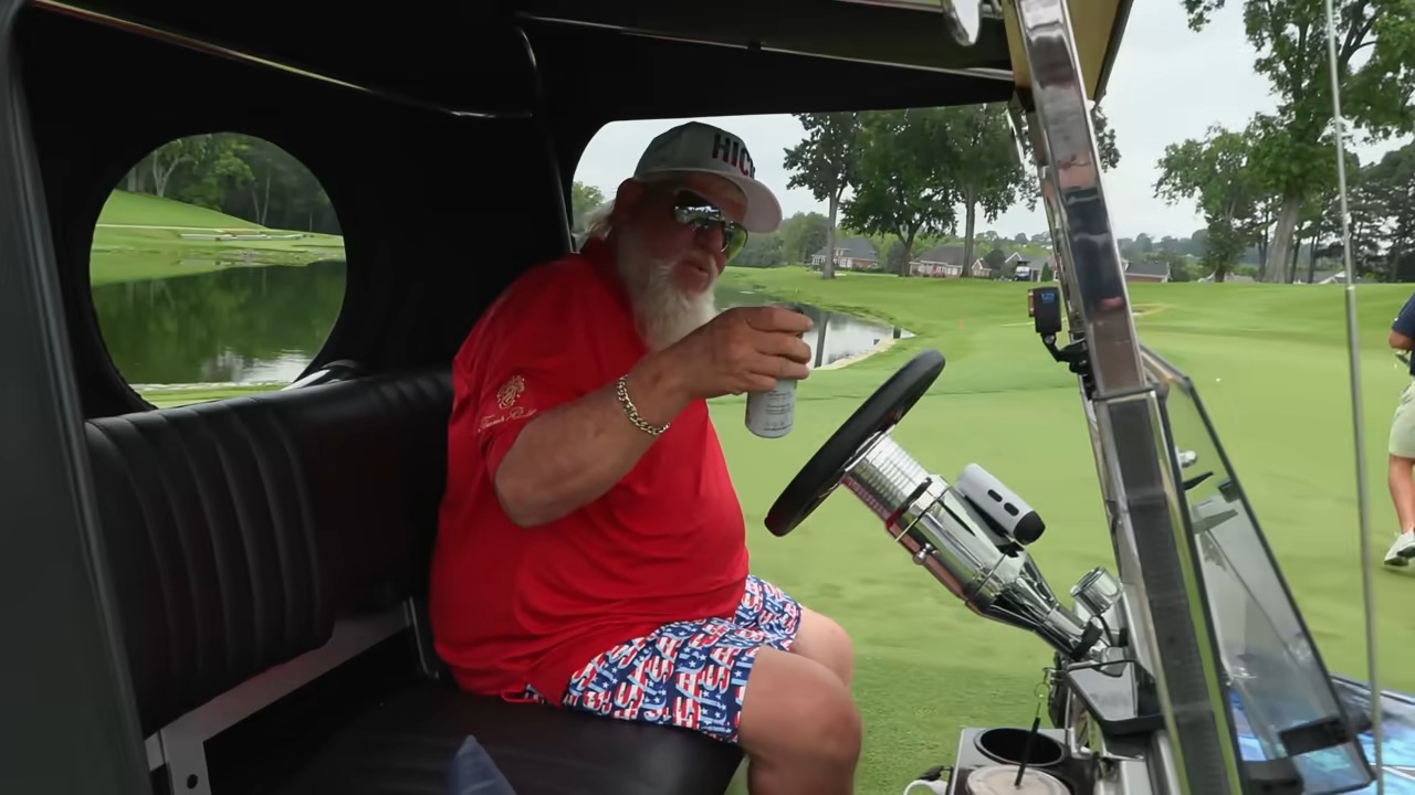 a man sitting in a golf cart holding a can of beer