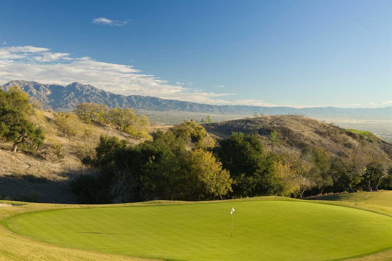 a green golf course with mountains in the background