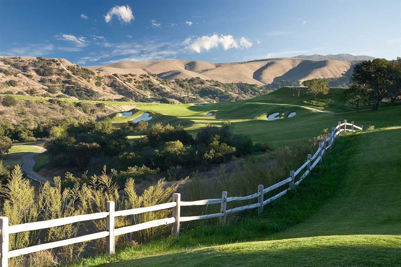 a white fence surrounds a golf course with mountains in the background