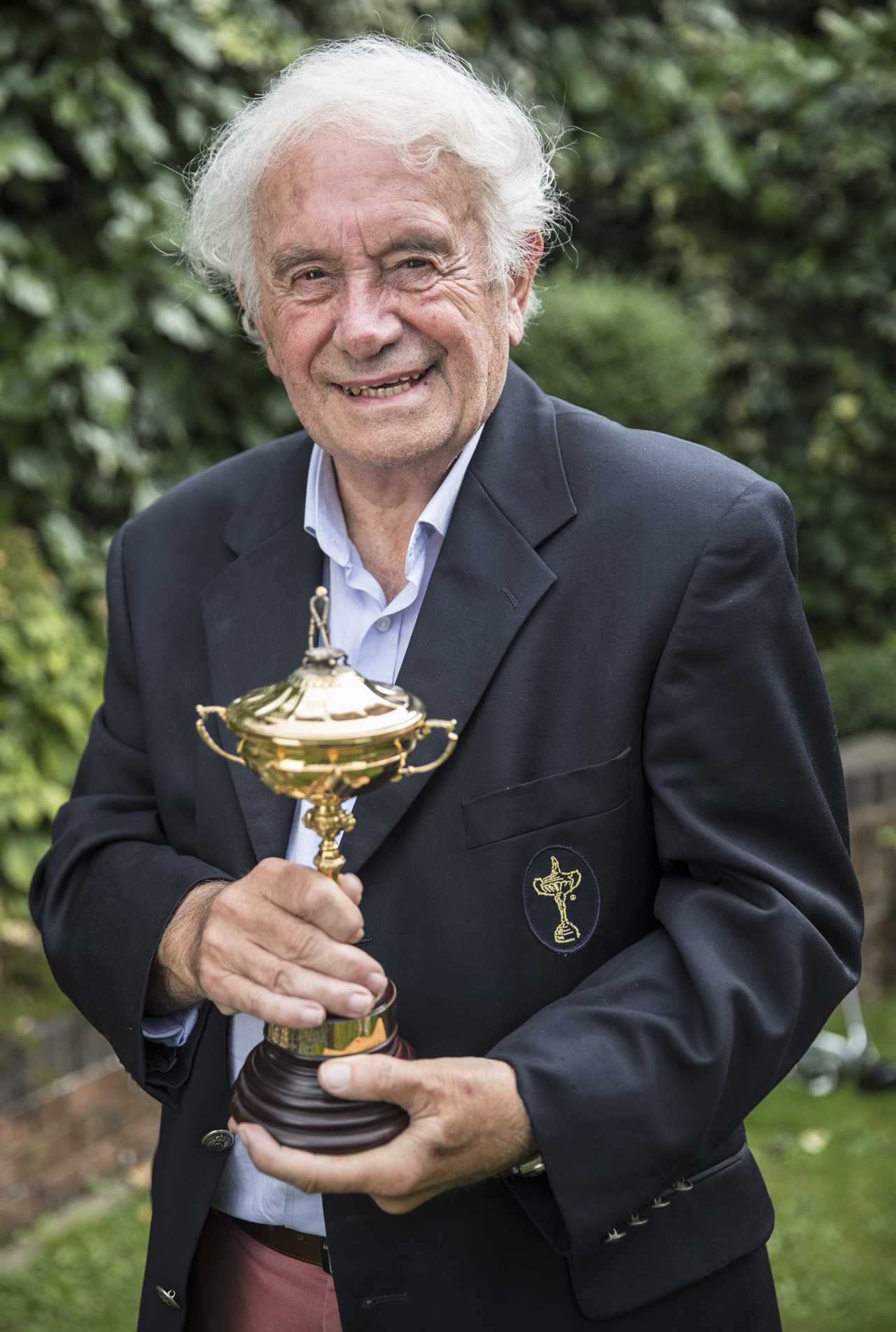 a man in a black jacket is holding a gold trophy