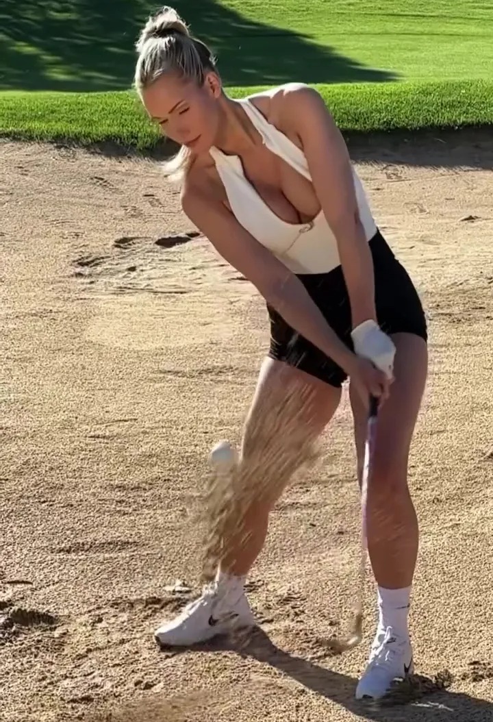 a woman is swinging a golf club on a sandy golf course