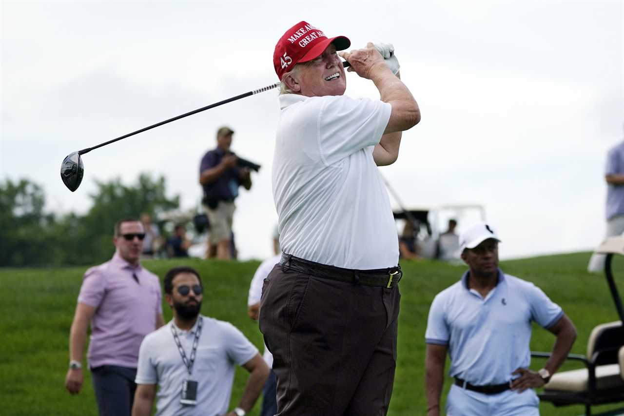 a man wearing a make america great again hat swings a golf club