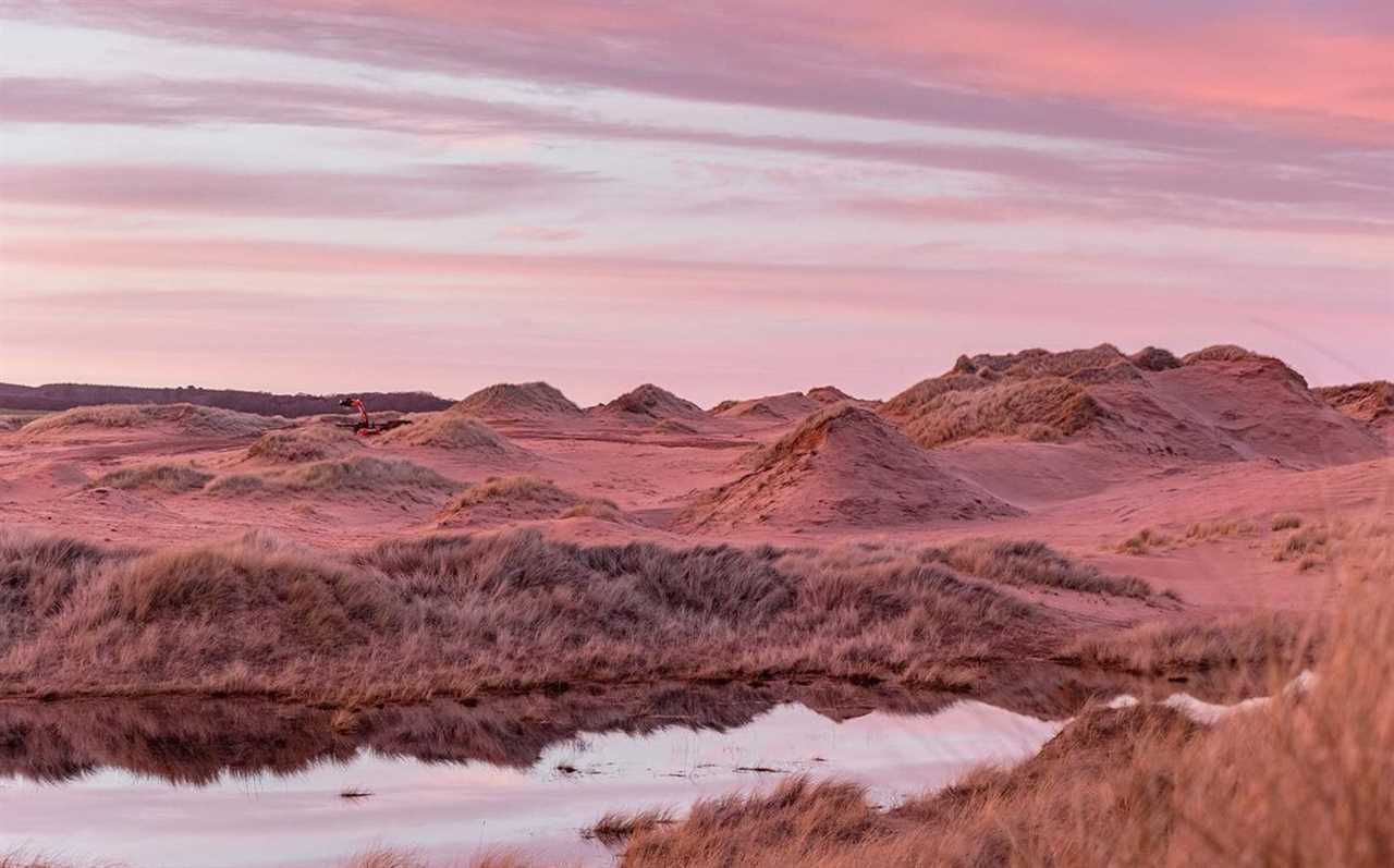 a sunset over a desert landscape with a small body of water in the foreground