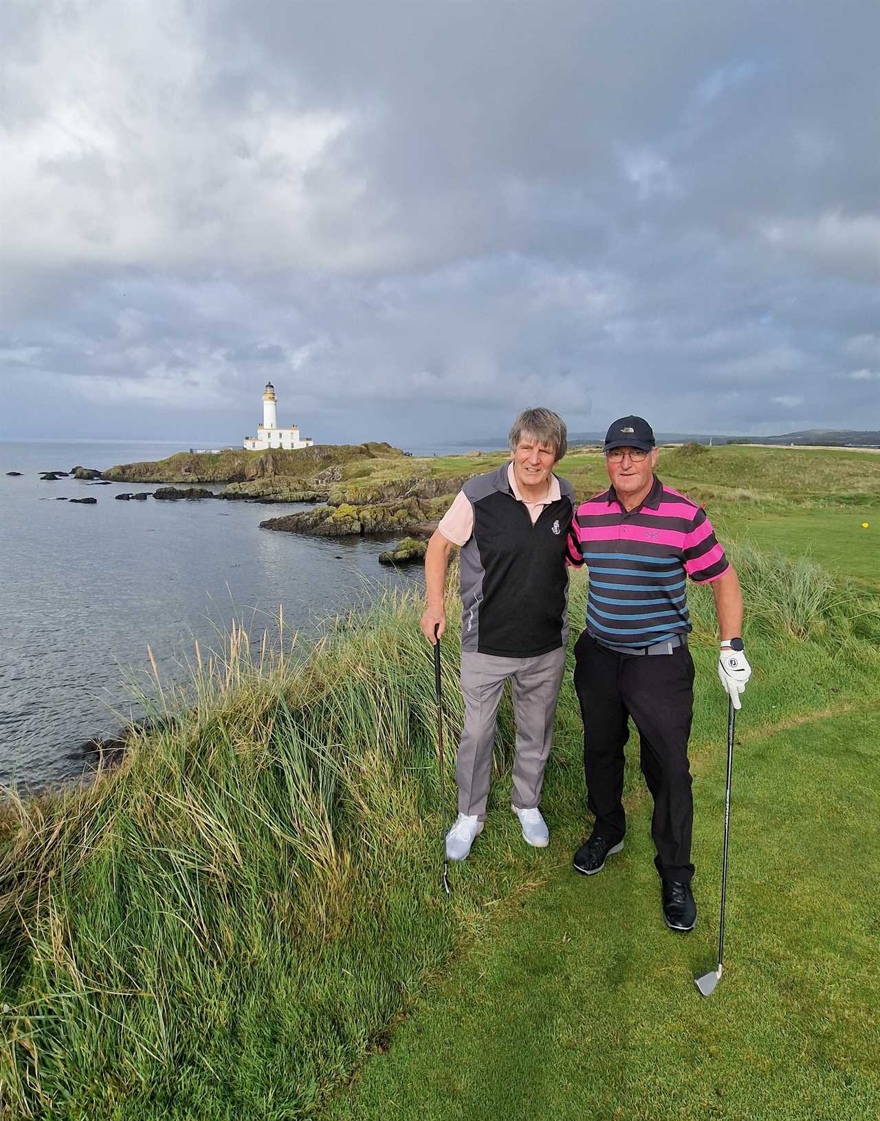 two men standing on a golf course with a lighthouse in the background