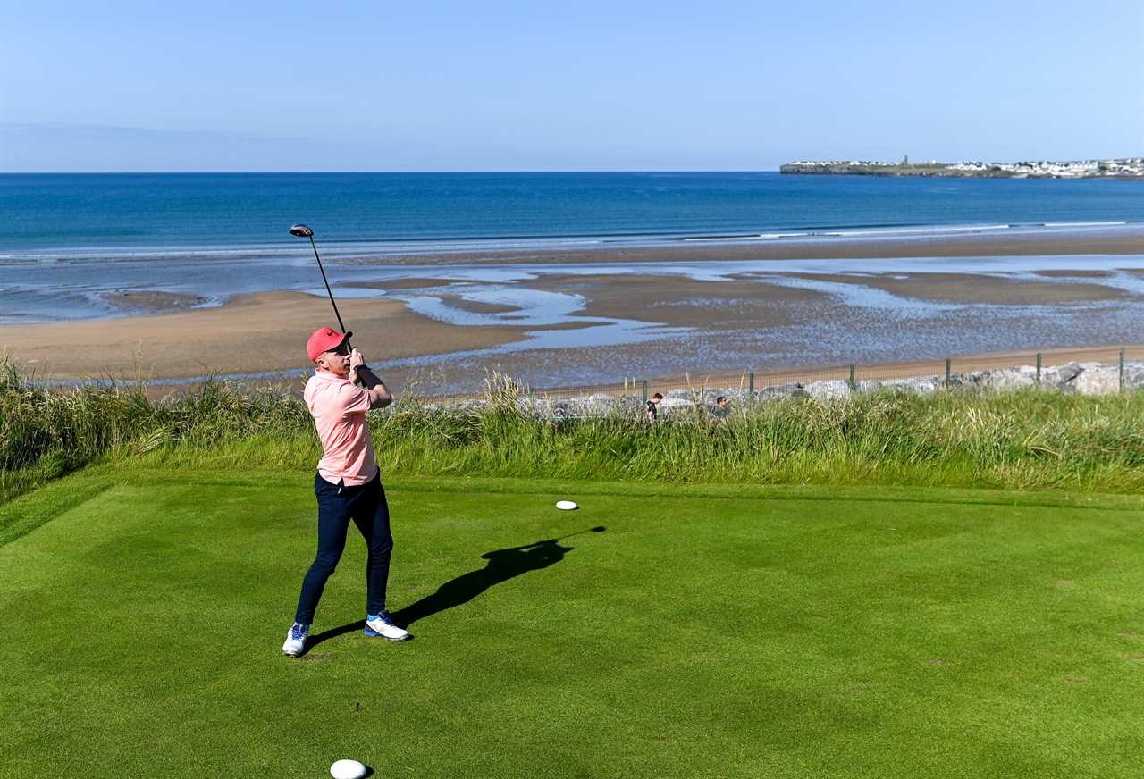 a man in a pink shirt is swinging a golf club on a golf course