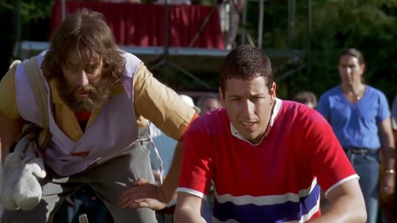 Adam Sandler and a bearded man in a golf cart.