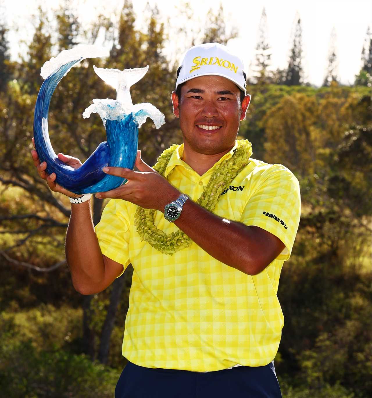 Hideki Matsuyama holding a whale tail trophy after winning a golf tournament.