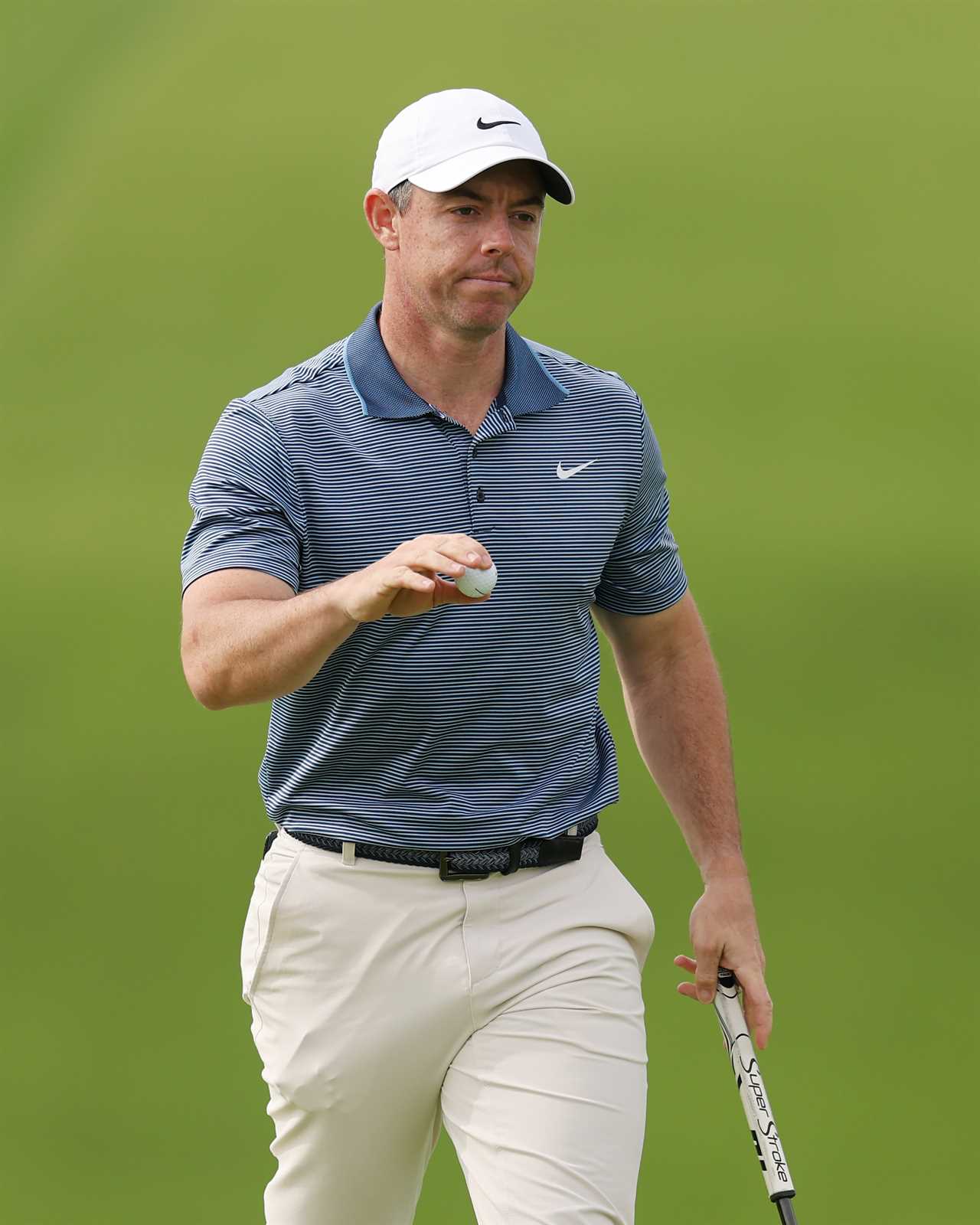 Rory McIlroy holding a golf ball on a golf course.