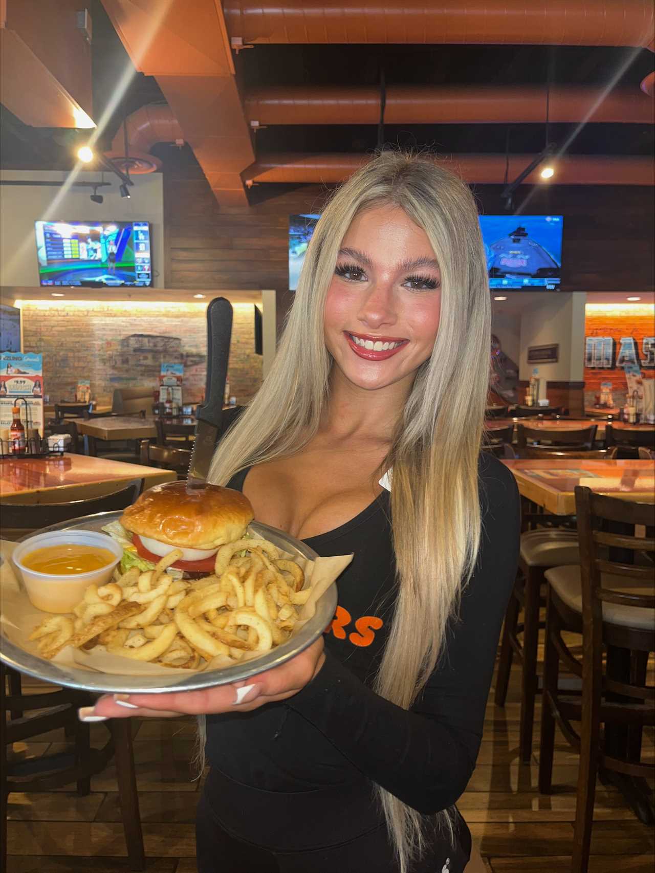 Woman in Hooters uniform holding a burger and curly fries.