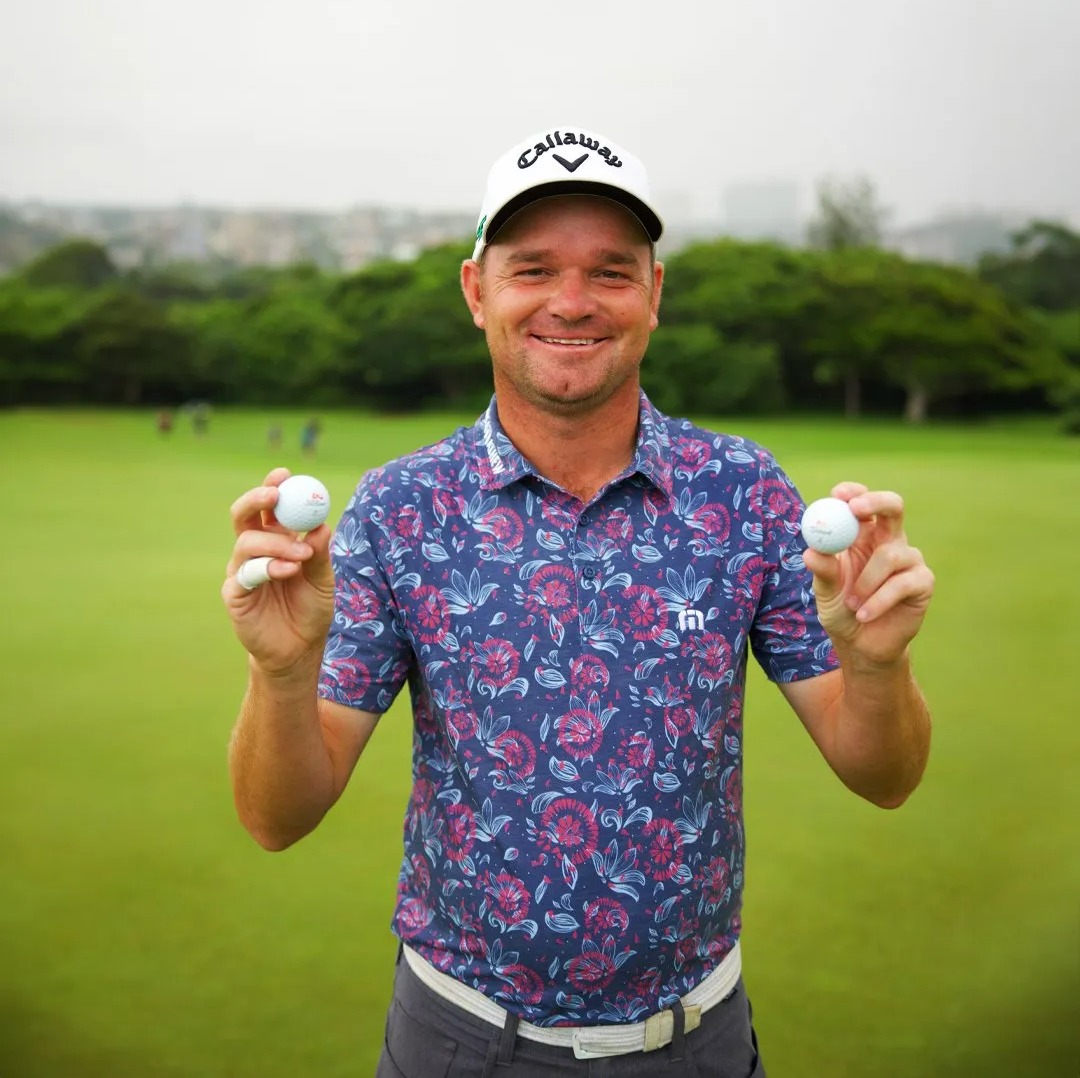 Golfer Dale Whitnell holding two golf balls after making two holes-in-one in one round.