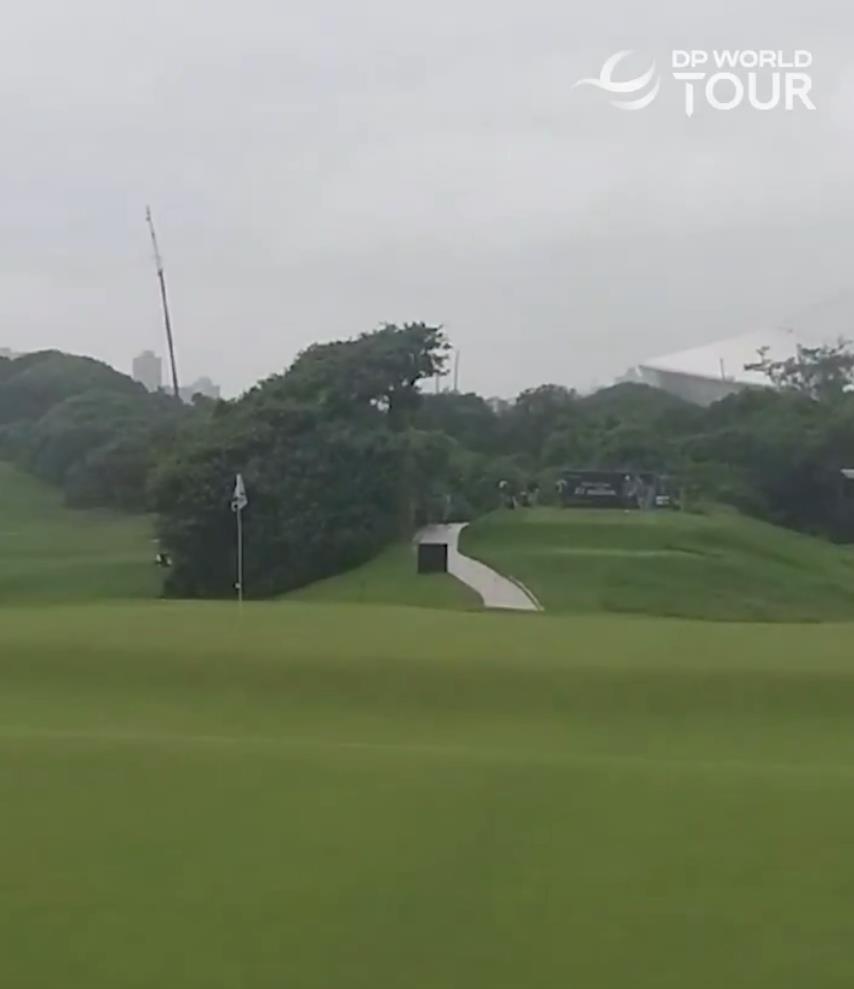 Rainy golf course with a flag in the distance.