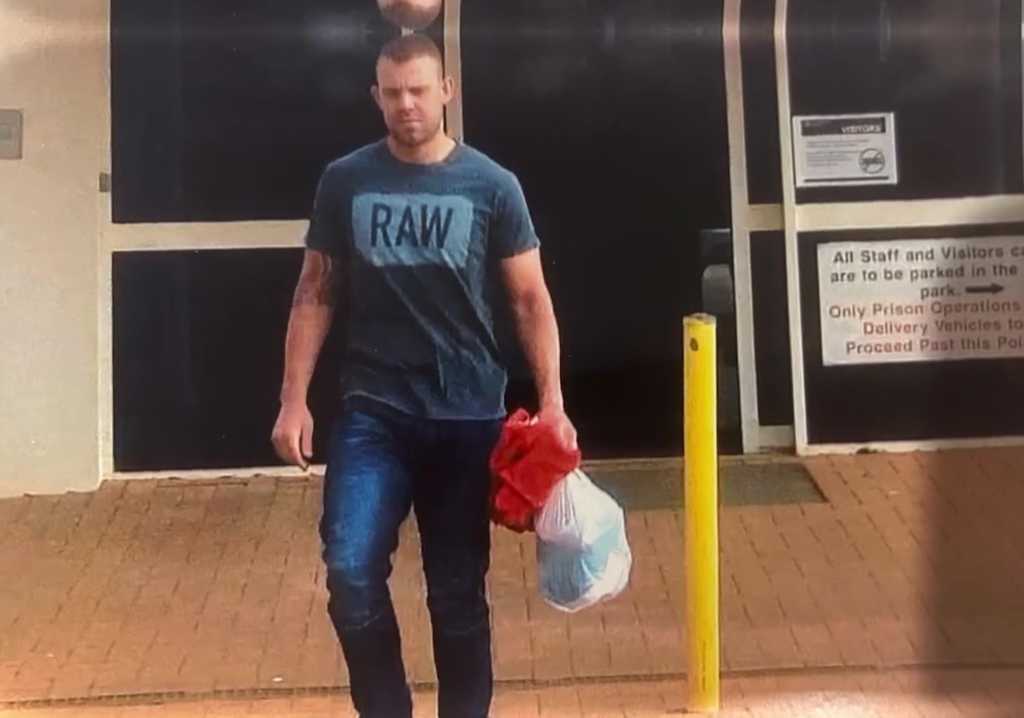 Man in RAW t-shirt carrying bags near a building.