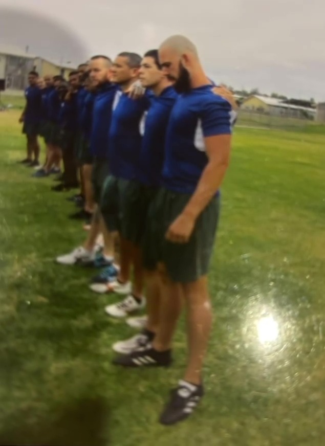 Group of men in blue shirts and green shorts standing on a grassy field.