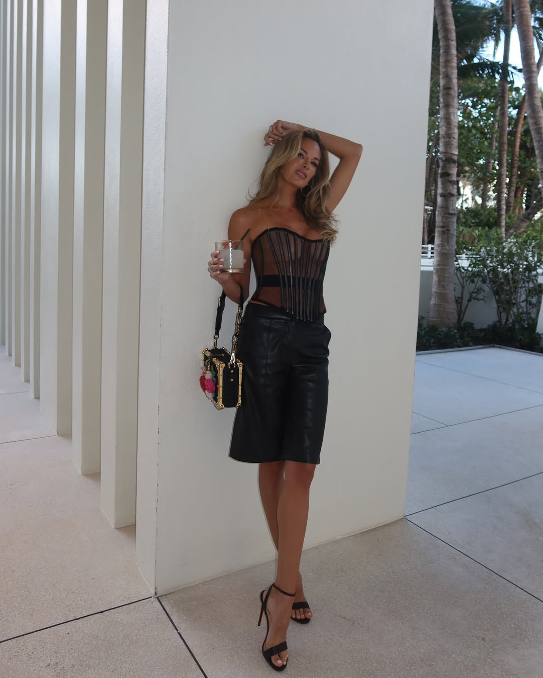 Woman in black corset and leather shorts holding a drink.