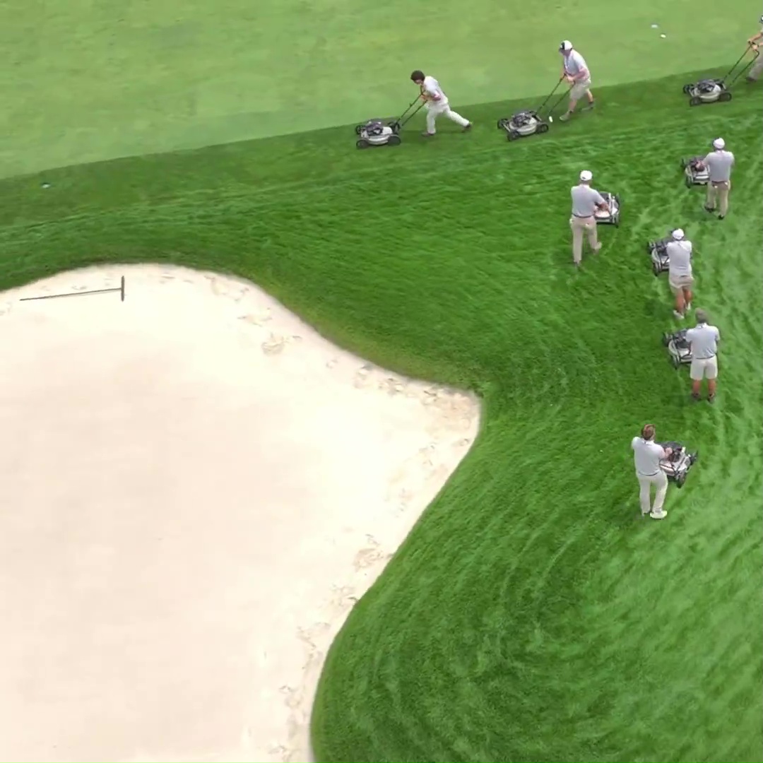 Aerial view of groundskeepers mowing a golf course.
