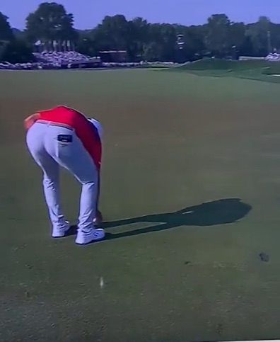 Golfer bending over on the green.