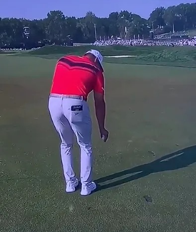 Golfer bending over on the green.