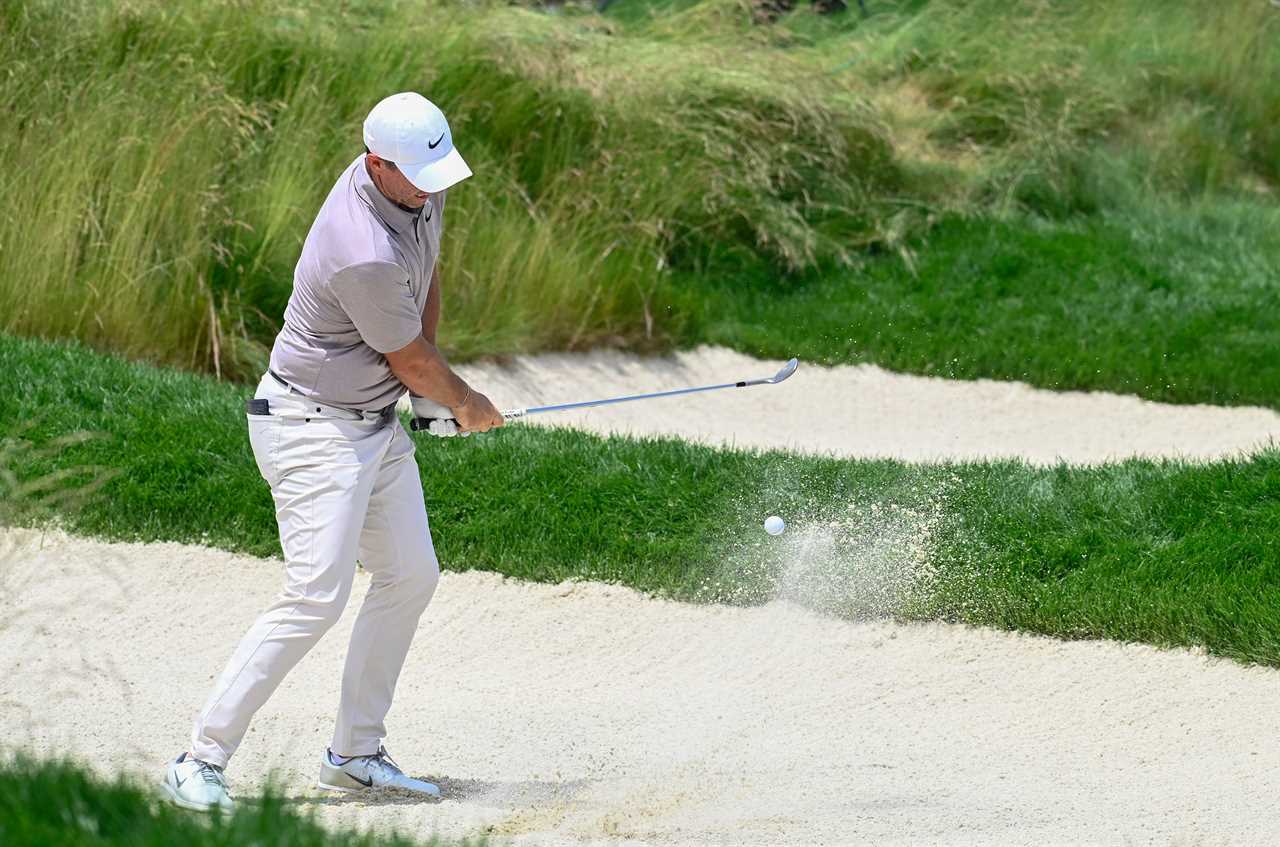 Rory McIlroy hitting a golf ball out of a sand trap.
