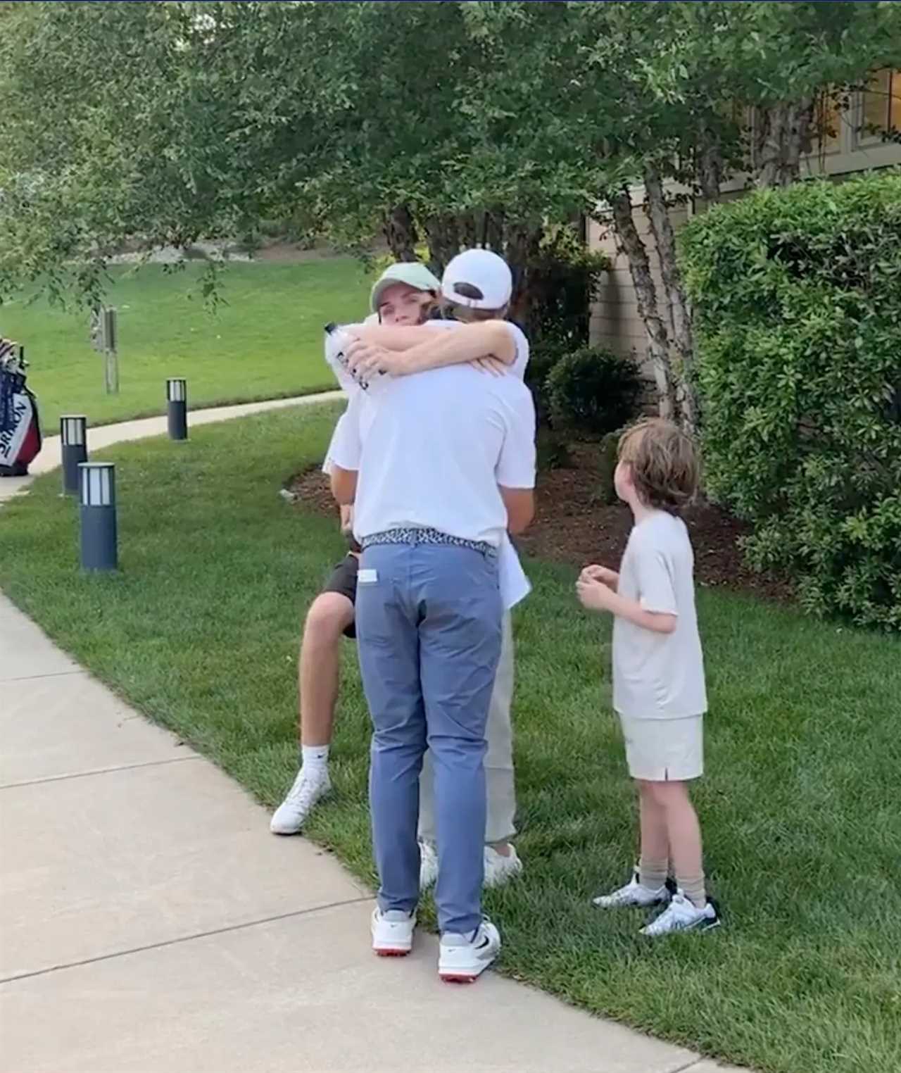 Screenshot of two people hugging while a young boy looks on.