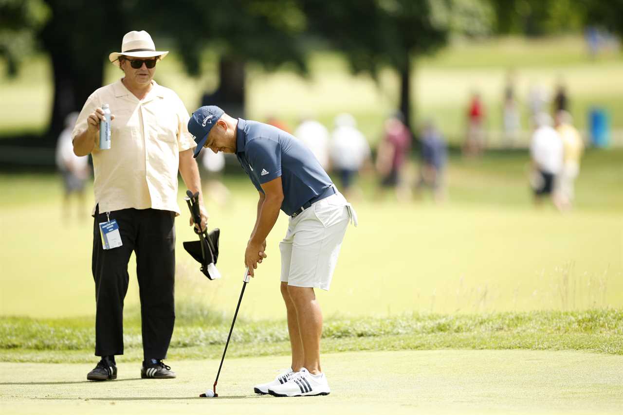 Xander Schauffele putting on the green, watched by his father.