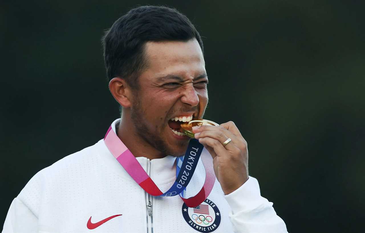 Xander Schauffele bites his gold medal at the Tokyo Olympics.