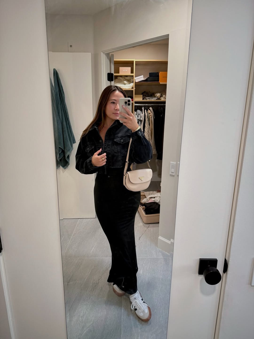 Woman in black denim jacket and maxi skirt taking a mirror selfie.