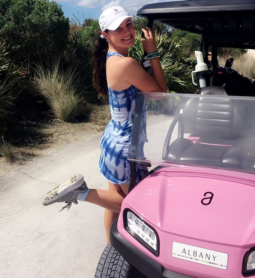 Woman in tie-dye dress posing with pink golf cart.