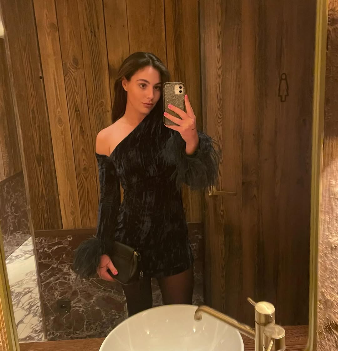 Woman in a dark velvet dress taking a selfie in a restroom.