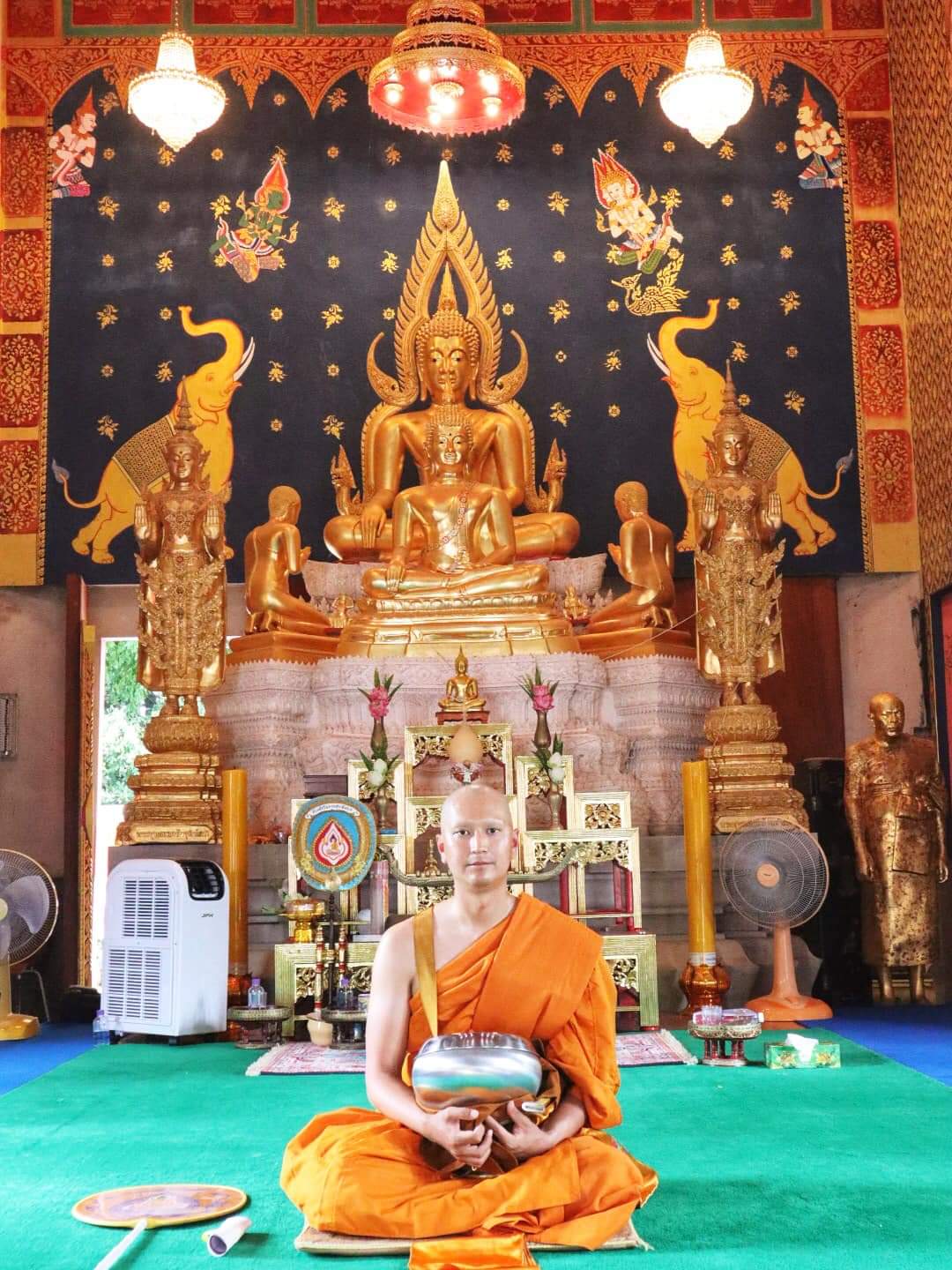 A Buddhist monk sits in a temple, holding a bowl.