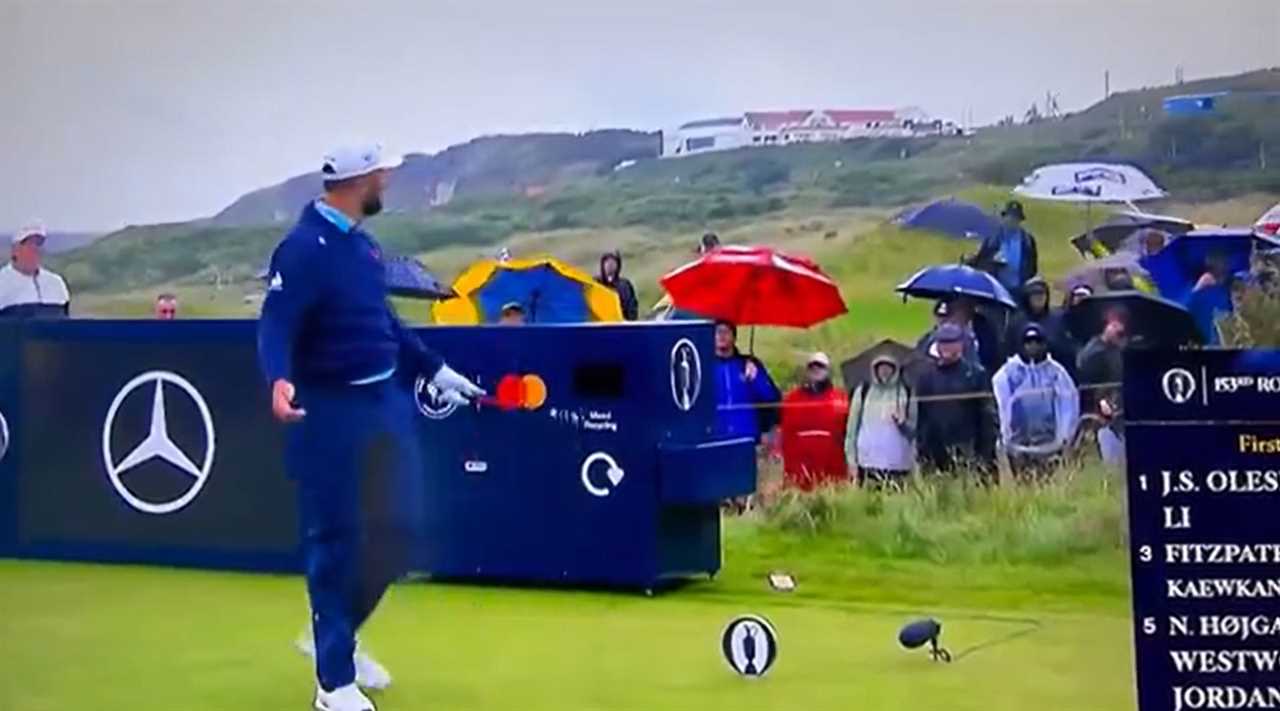 Golfer on a golf course teeing off near spectators with umbrellas.