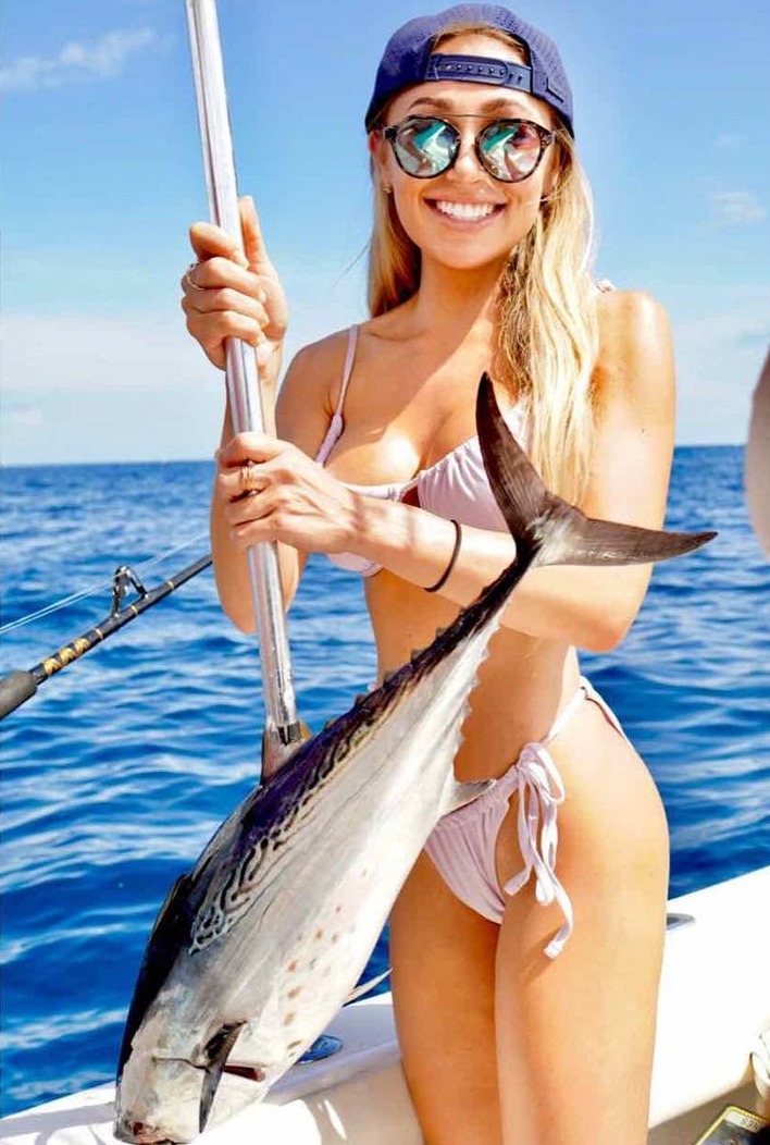 Woman in bikini holding a large fish on a boat.