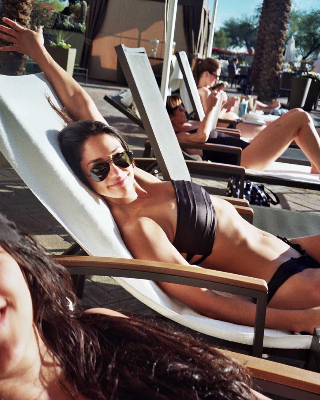 Woman in sunglasses relaxing on a lounge chair by a pool.