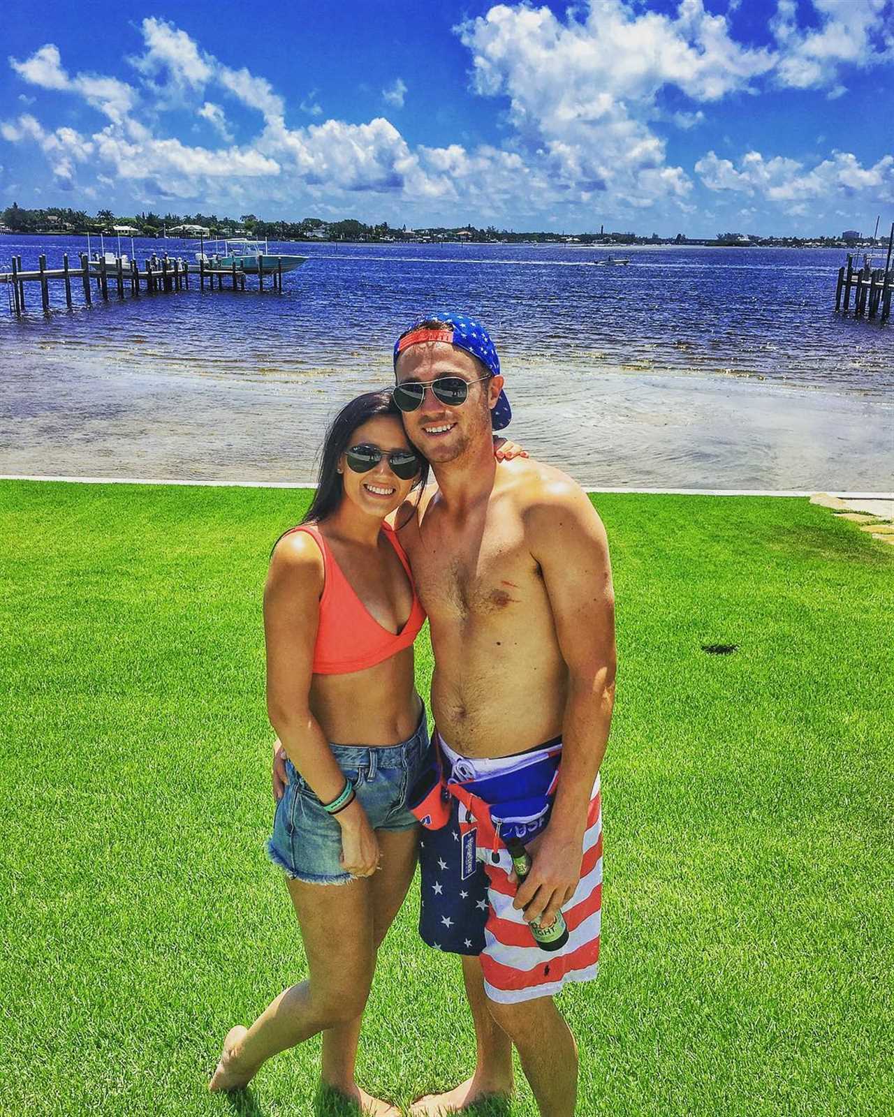 Couple posing on a grassy lawn by the water.