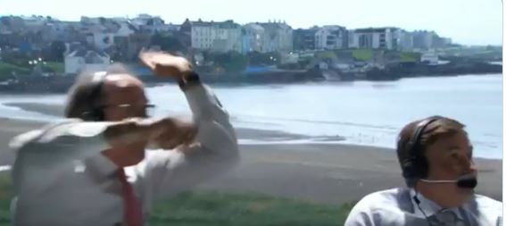 Man shielding his face from the wind, another man in the background.