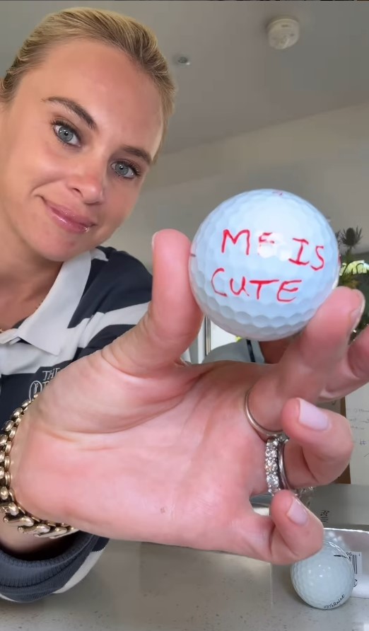Woman holding a golf ball with "Me is cute" written on it.