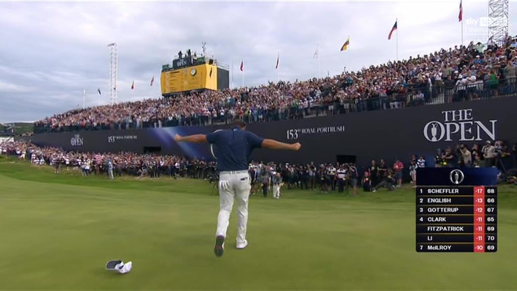 Golfer celebrating on the green with a large crowd cheering in the background.