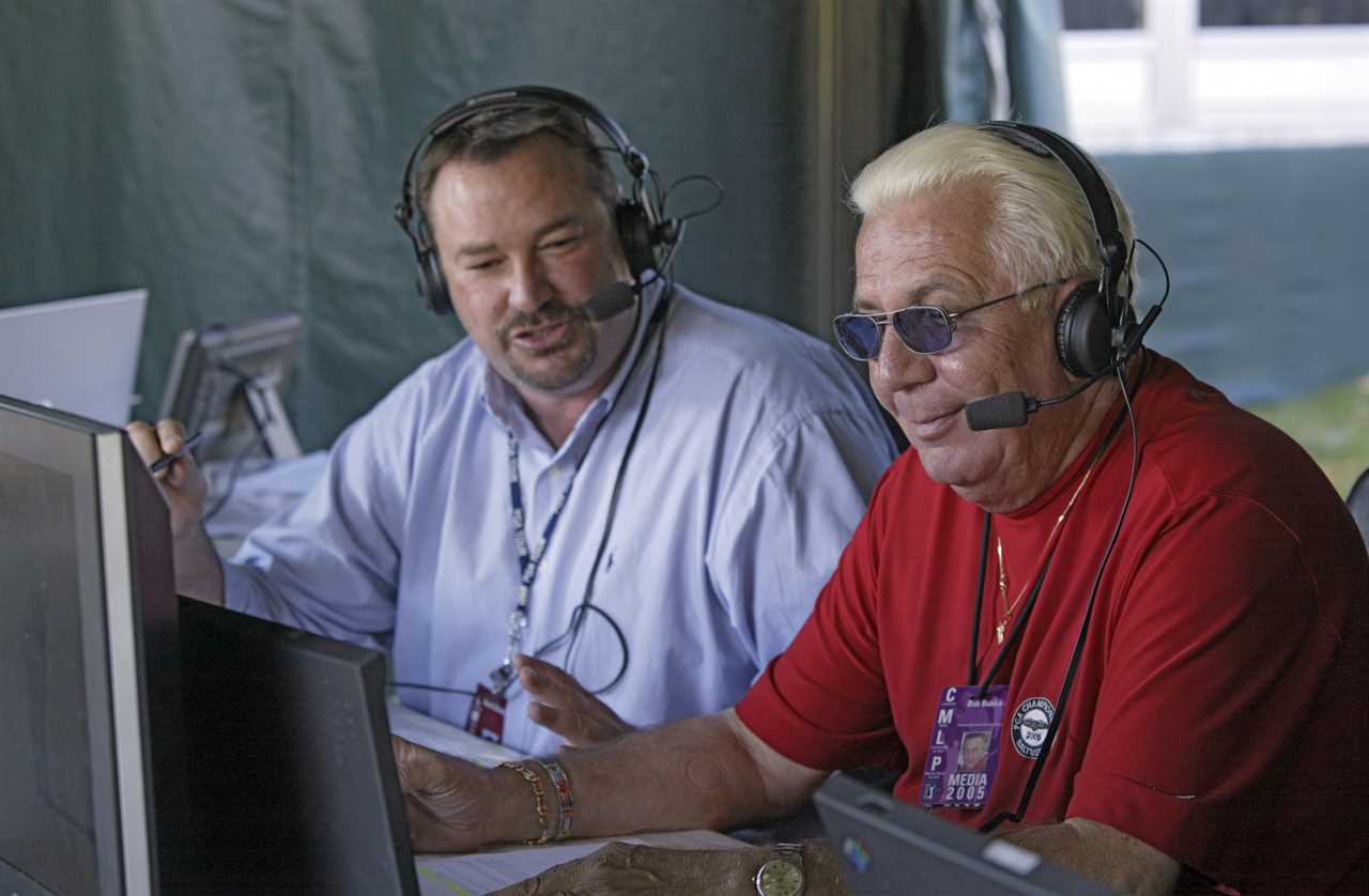 Two radio announcers at a golf tournament, wearing headsets and looking at computers.
