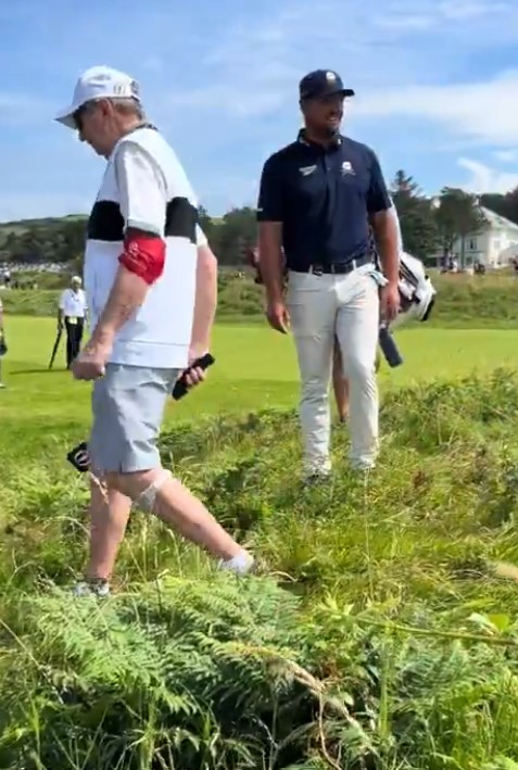 Two golfers walking across a grassy area.