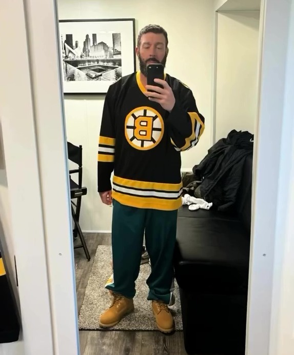 A man in a Boston Bruins jersey and Timberland boots taking a selfie.