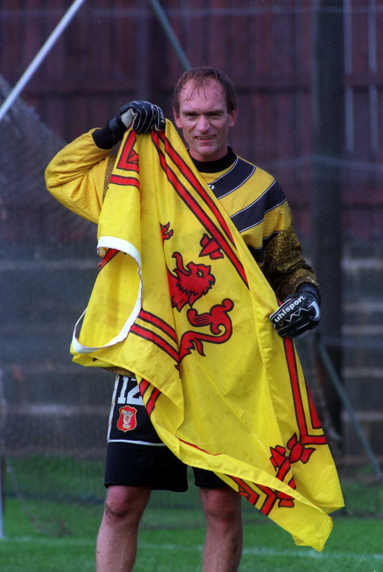 A soccer goalie holds up a Scottish flag.