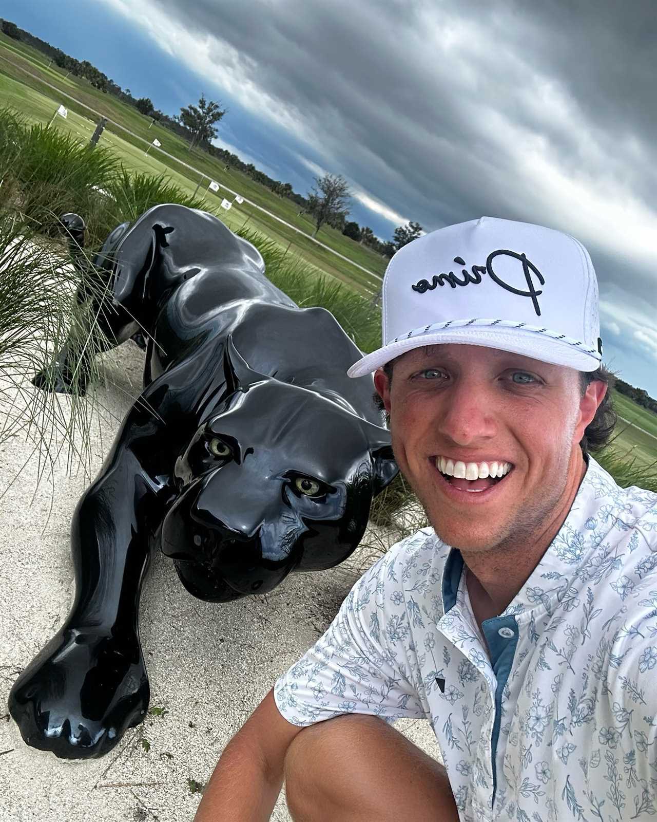 Man crouching by a black panther statue on a golf course.