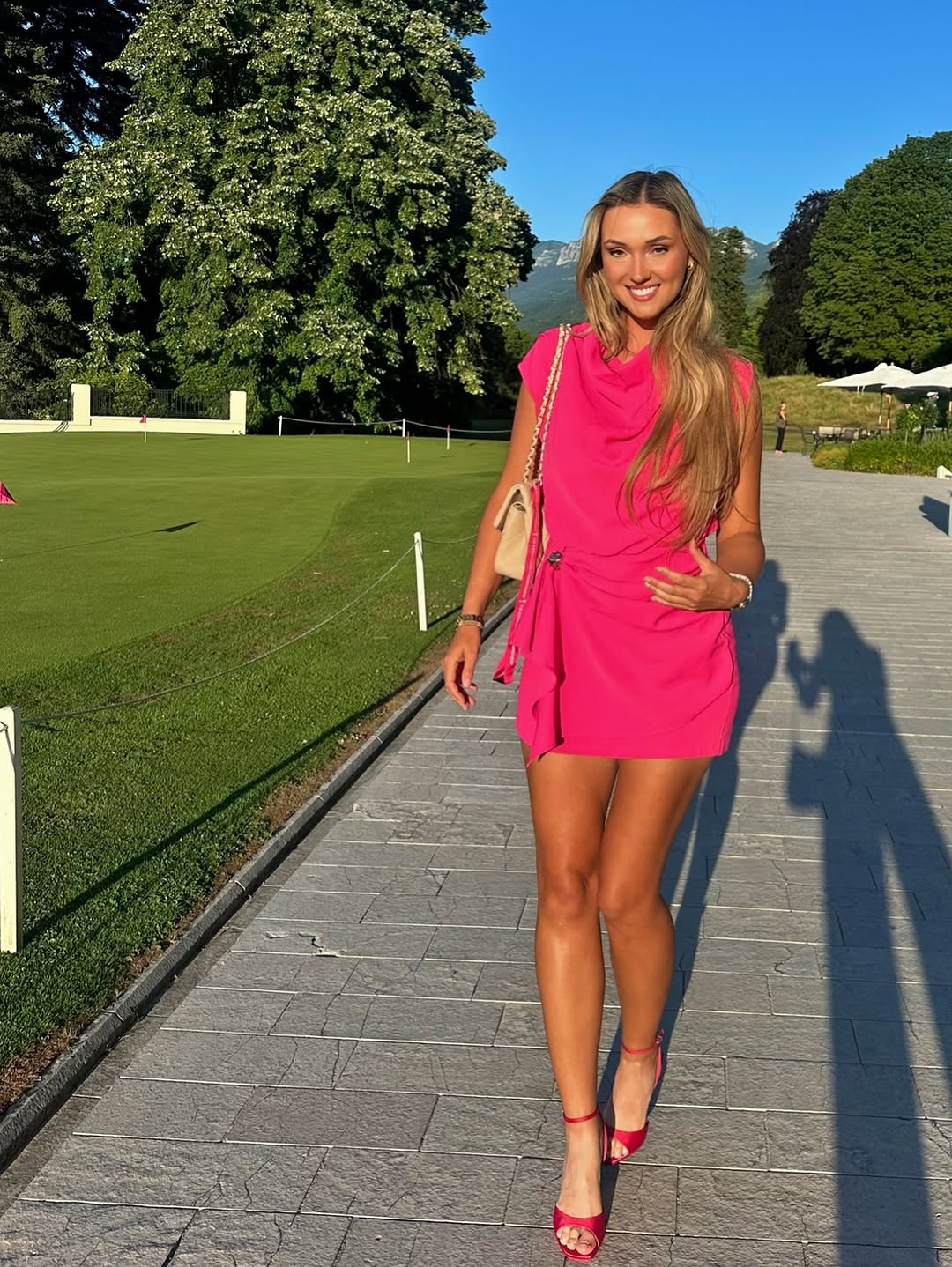 Woman in pink dress walking on path near golf course.